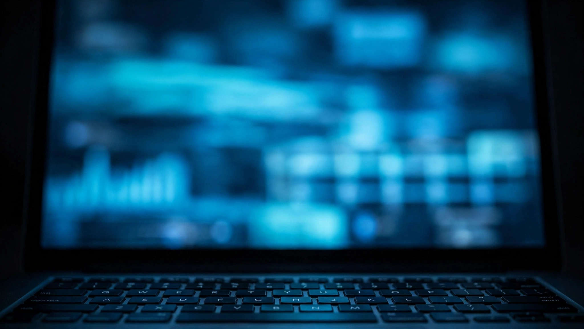 A laptop in a dark room with a blurred data interface on its screen