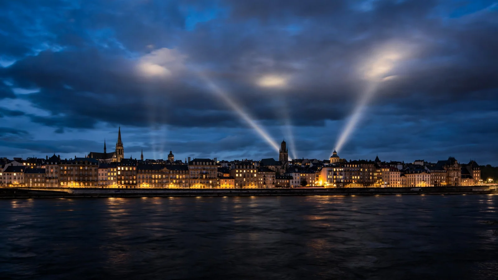 A European city skyline across a dark river at night, with searchlight beams sweeping through the clouds.