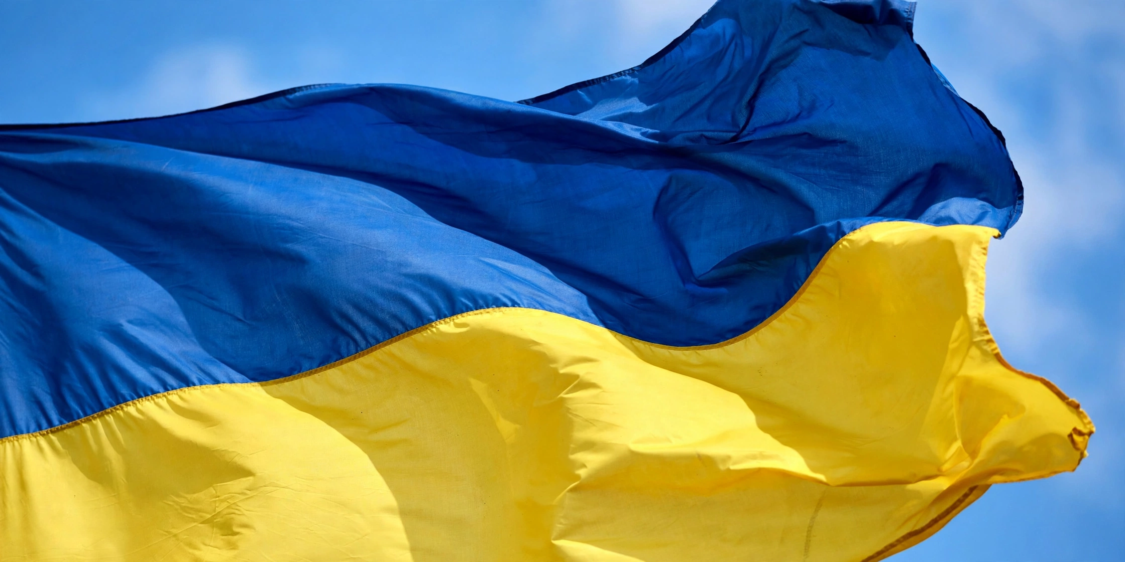 A blue-and-yellow Ukrainian flag waving against a blue sky.