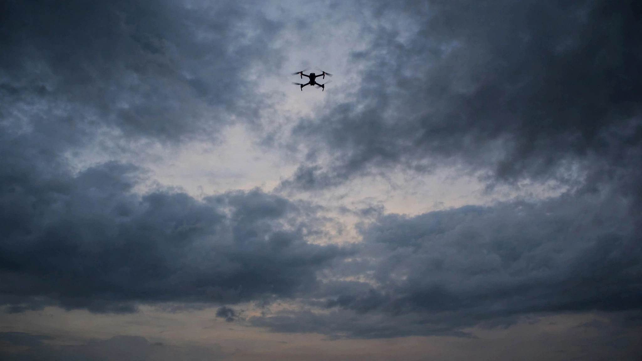 A small drone silhouetted against a cloudy sky at dusk.