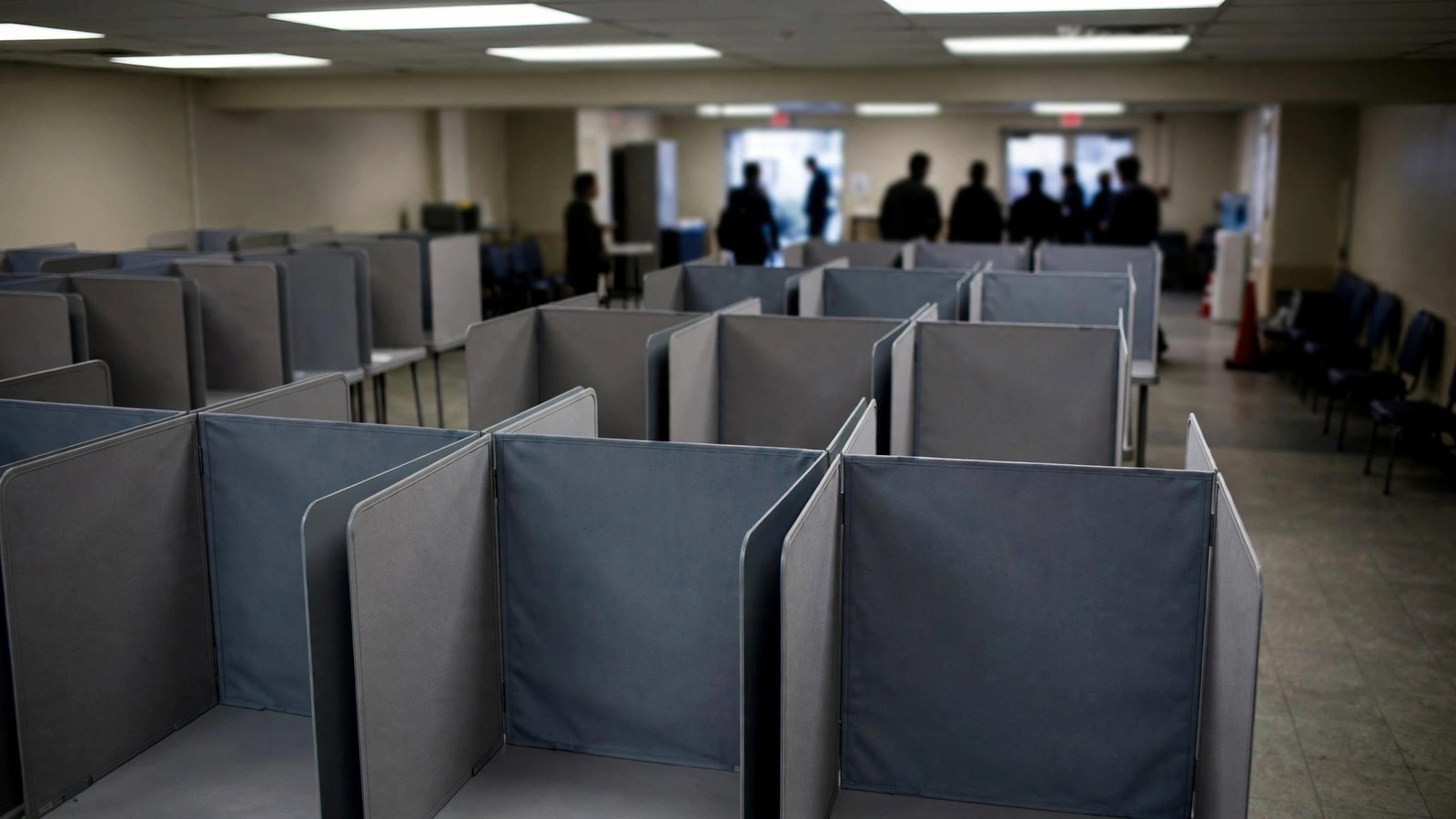 Rows of empty voting booths with privacy screens inside a polling place