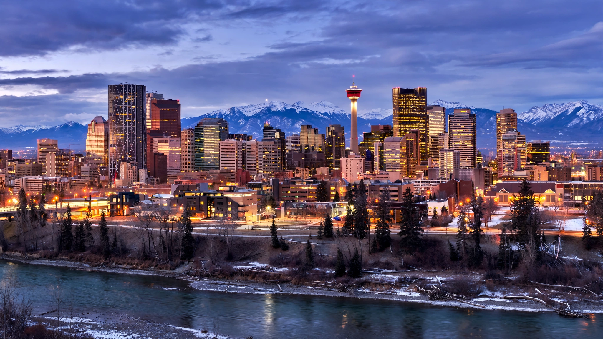The Calgary skyline at dusk with snow-capped mountains in the background.