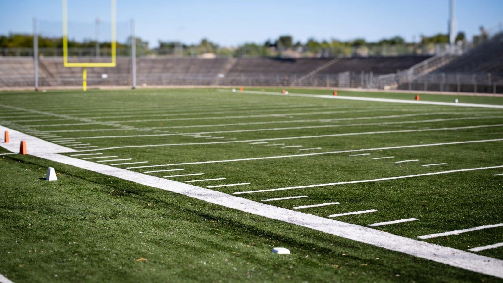 An empty football field with white yard lines and goal posts in the distance.
