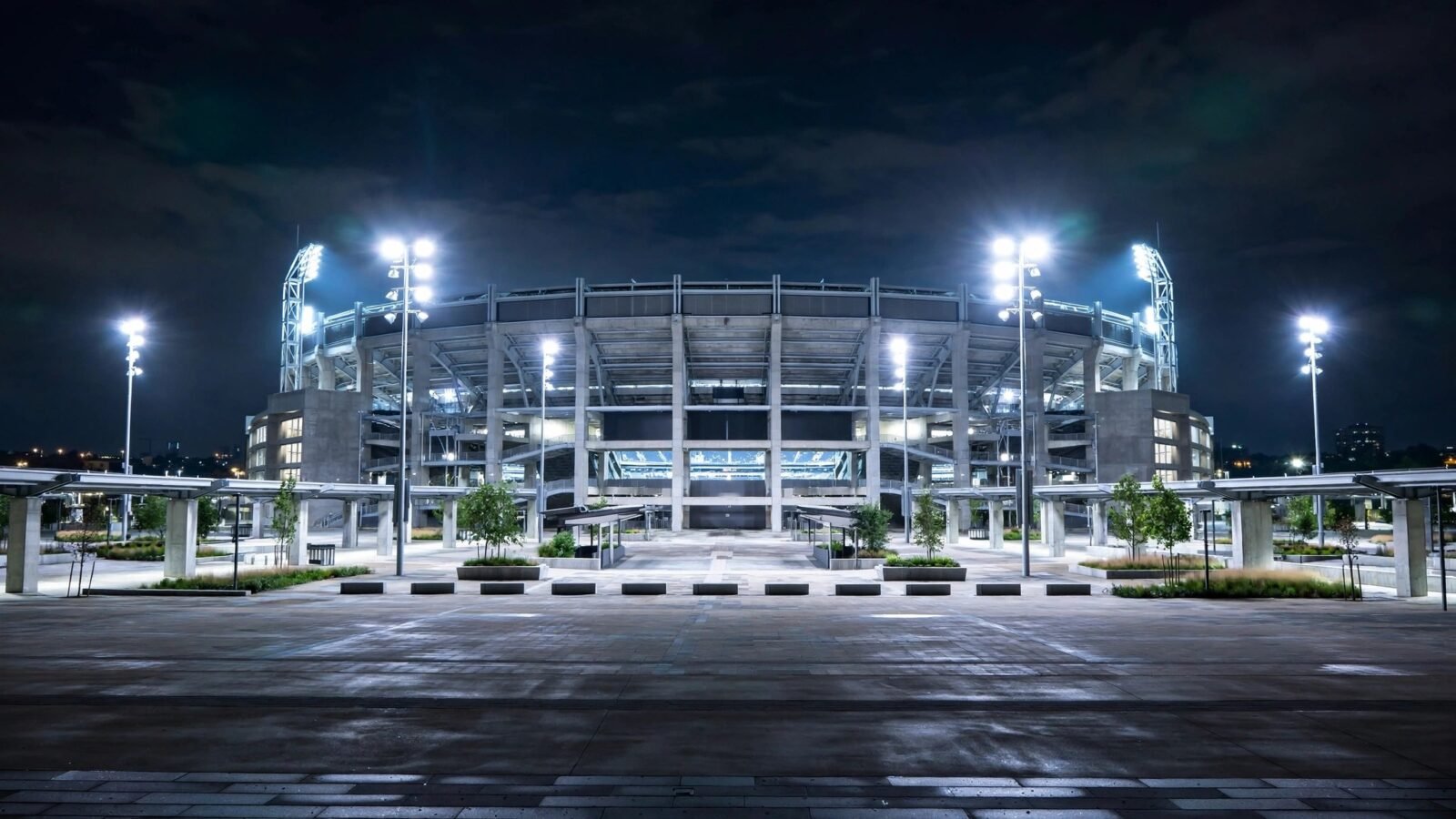 A large football stadium lit by floodlights at night, seen from an empty plaza.