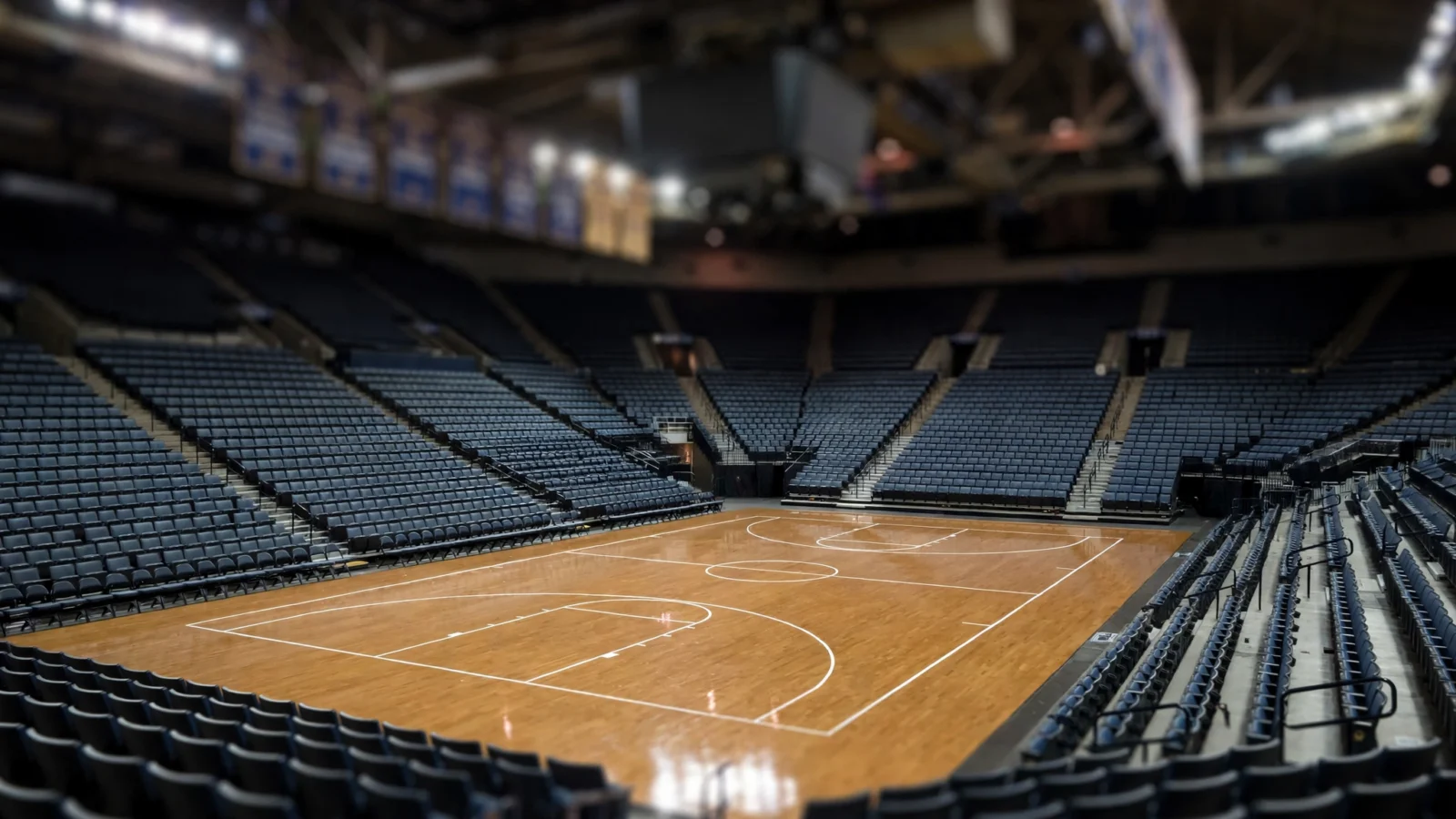 An empty college basketball arena with a polished hardwood court under overhead lights