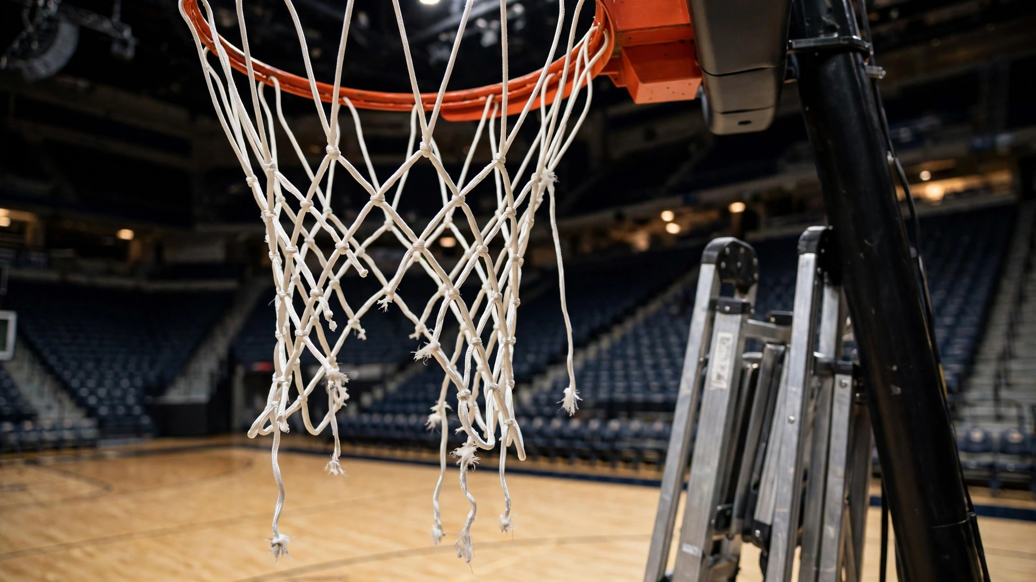 A basketball hoop and net seen over an empty court, with a folded ladder beside the basket