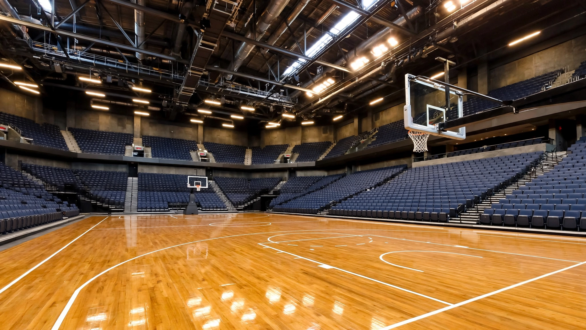An empty indoor basketball arena with a polished wooden court and hoops