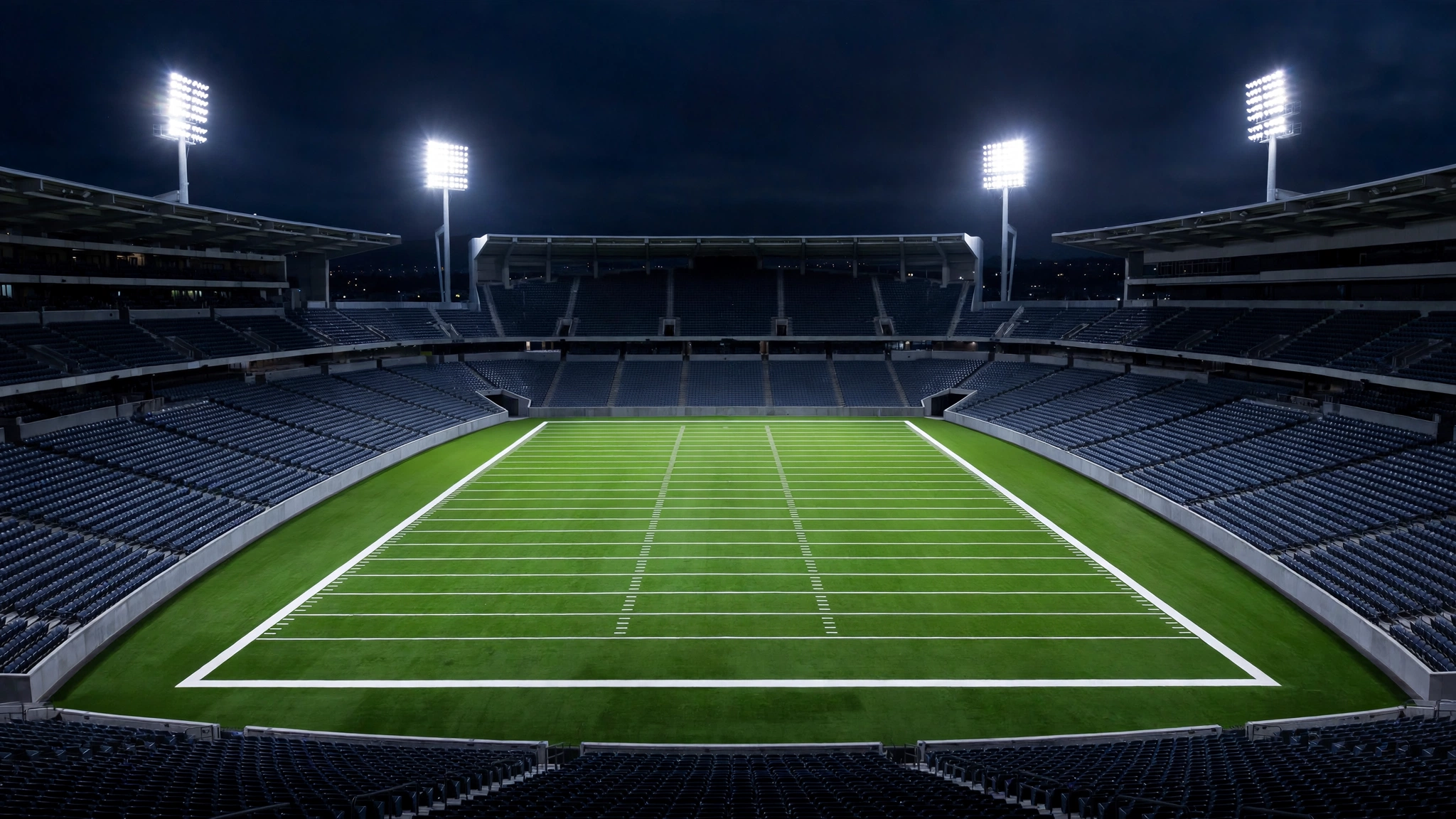 An empty football stadium at night with a lit green field and white yard lines