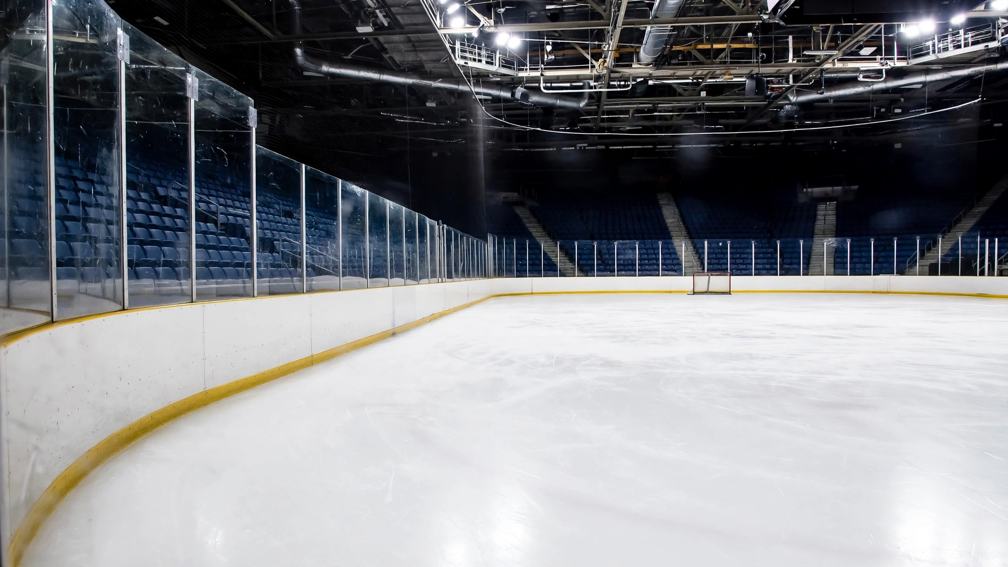 An empty indoor ice hockey rink with boards, glass and arena seating