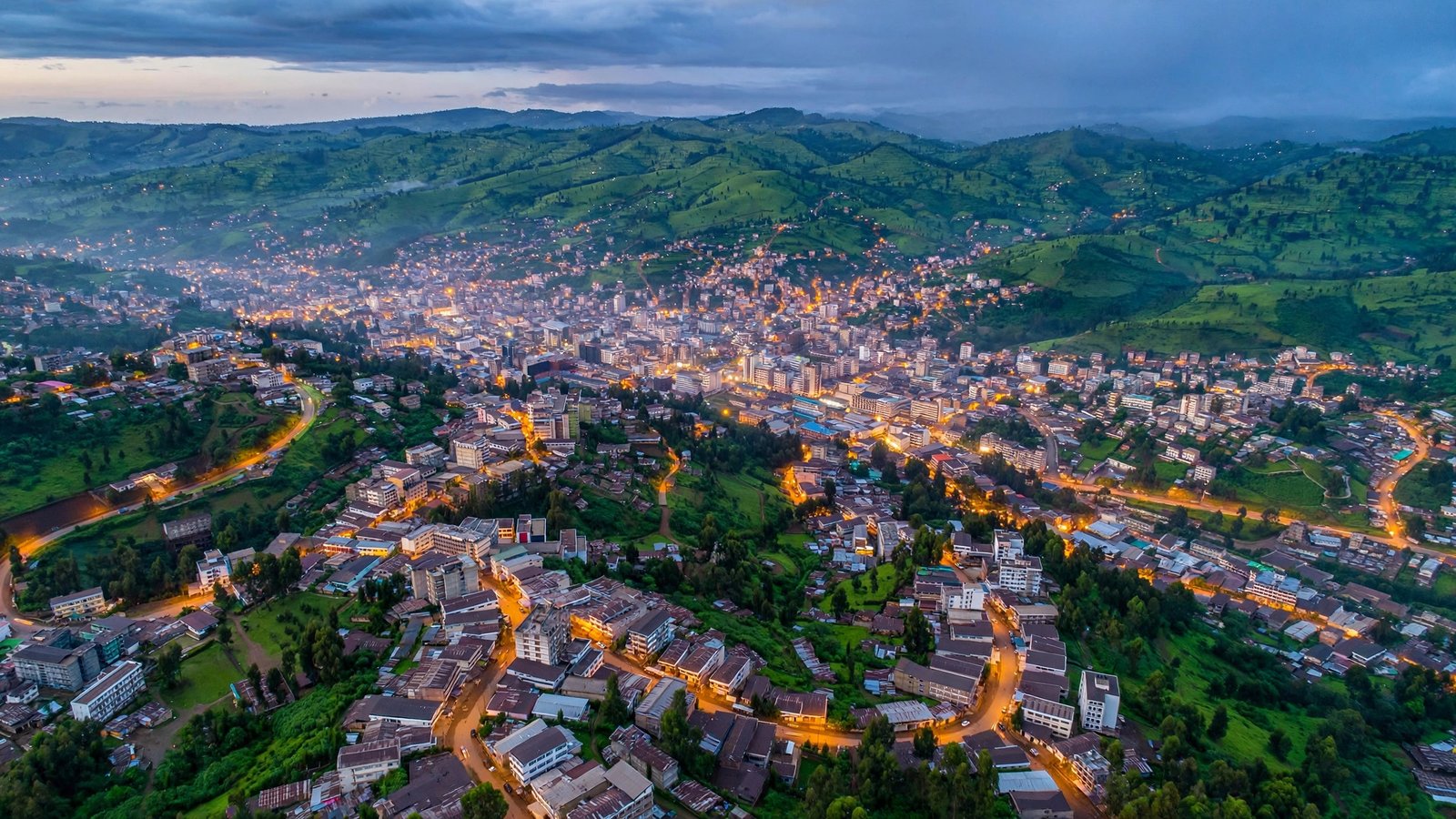 Aerial view of an East African capital city among green hills at dusk, city lights coming on