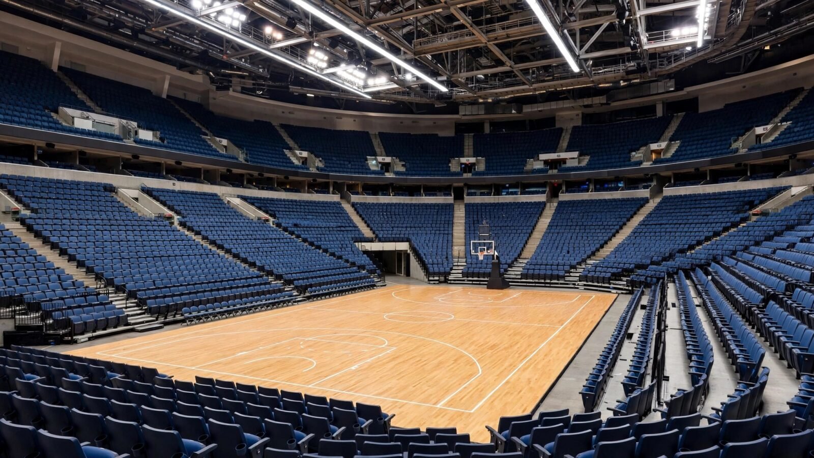 An empty professional basketball arena with blue seats and a polished hardwood court under bright lights.