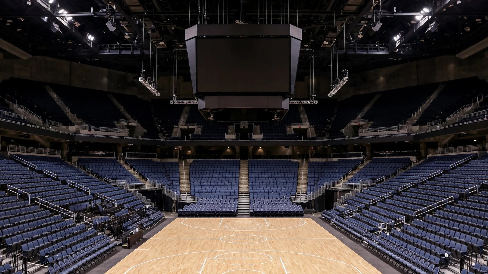 Empty blue arena seats and a dark scoreboard above a basketball court.