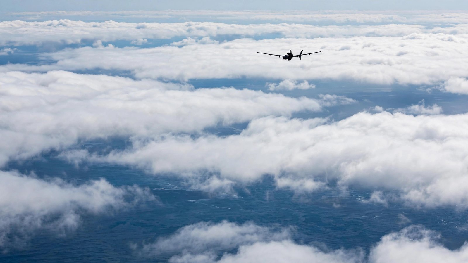 A military surveillance drone flying high above clouds over the sea