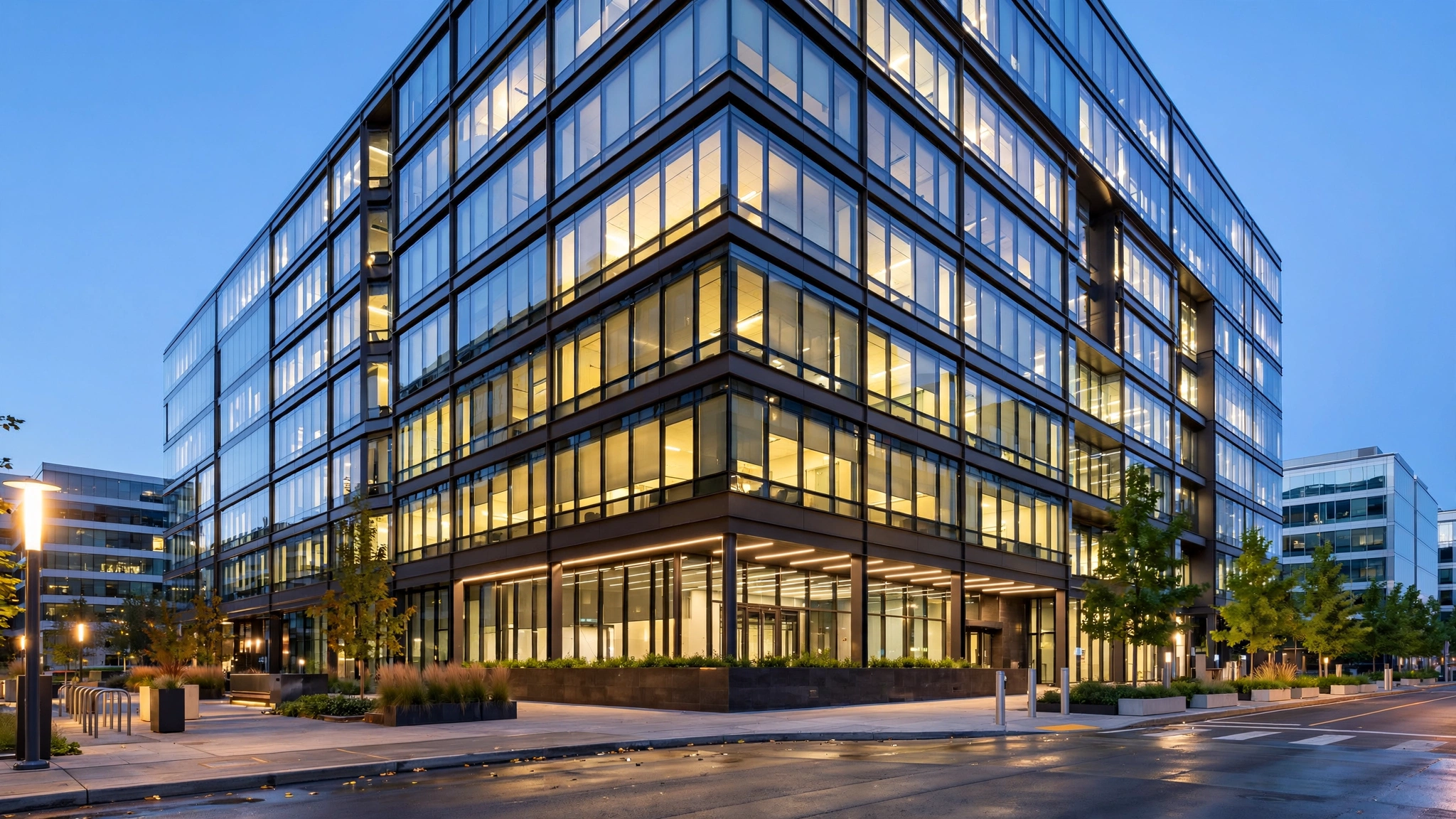 A glass corporate office building photographed from the street at dusk