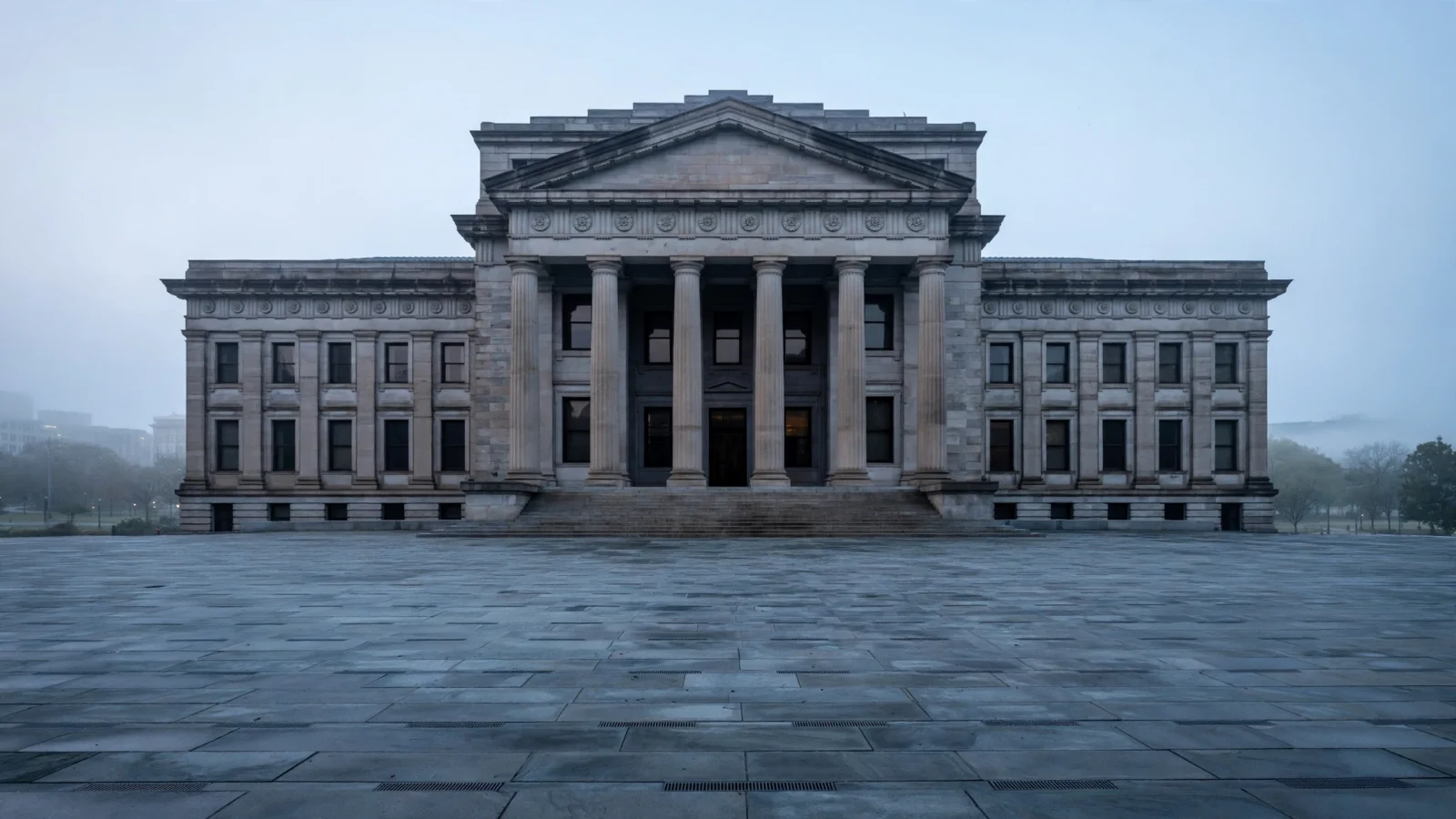 A neoclassical stone courthouse with tall columns behind an empty paved plaza in morning light