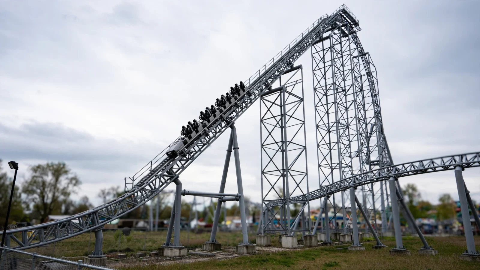 A tall steel roller coaster with a train of riders climbing a steep lift hill under a cloudy sky