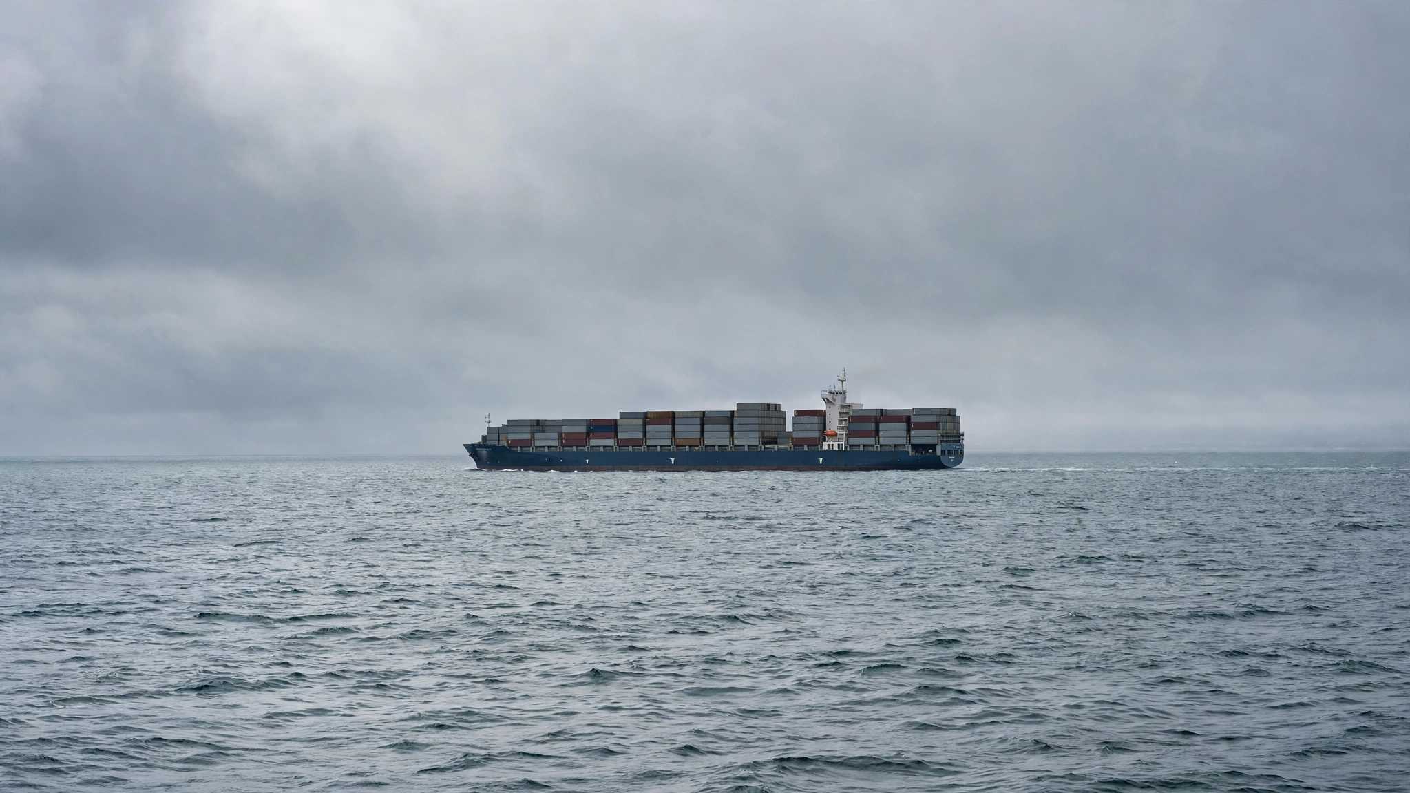 A large container cargo ship sailing on open sea under a grey sky