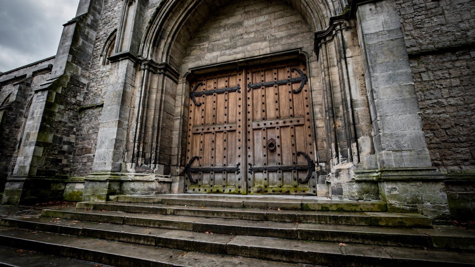 Large wooden double doors with iron hinges at the top of stone steps at a cathedral entrance