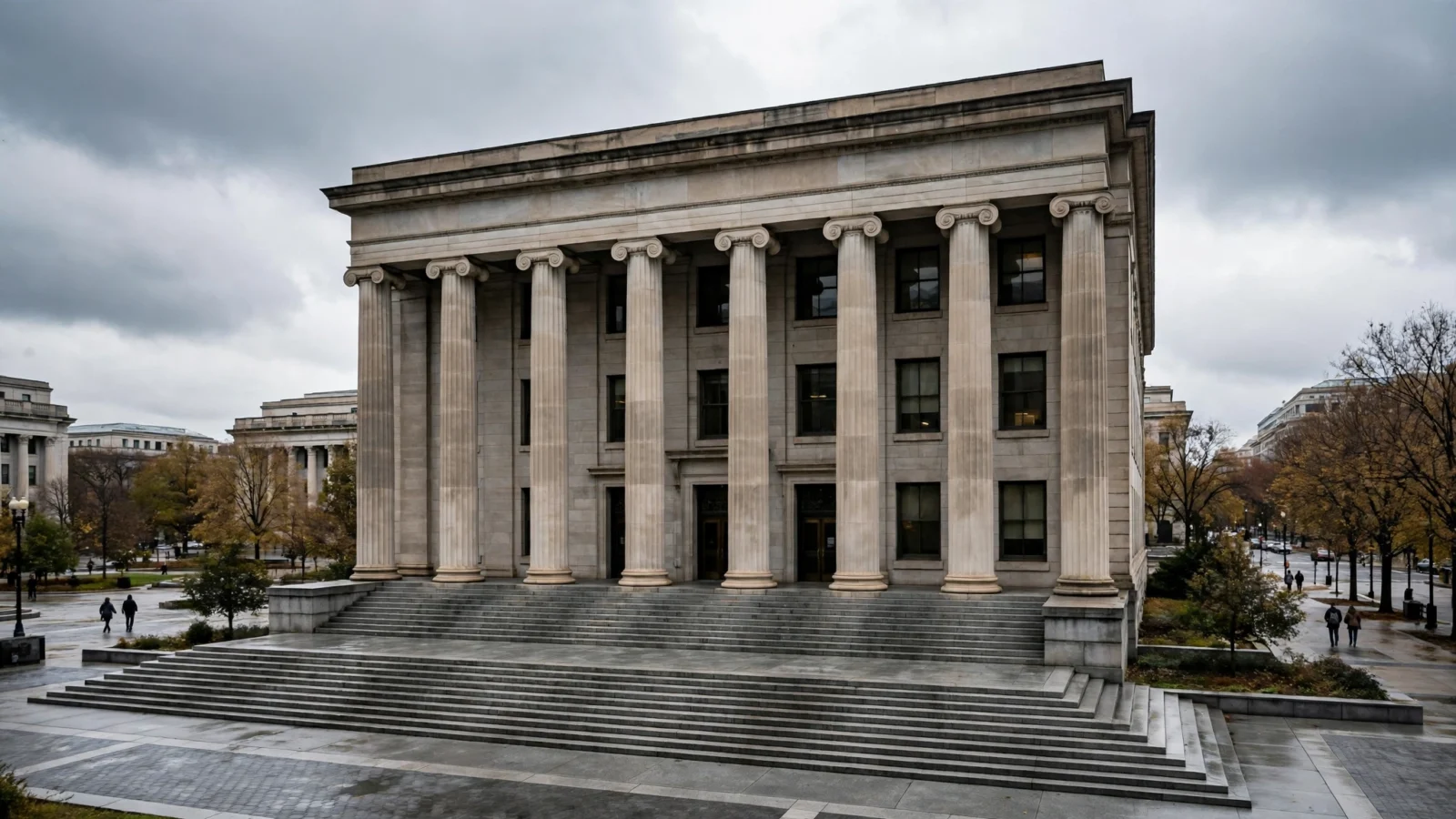 Stone courthouse building with tall columns and wide steps under a cloudy sky, with a few people walking at a distance