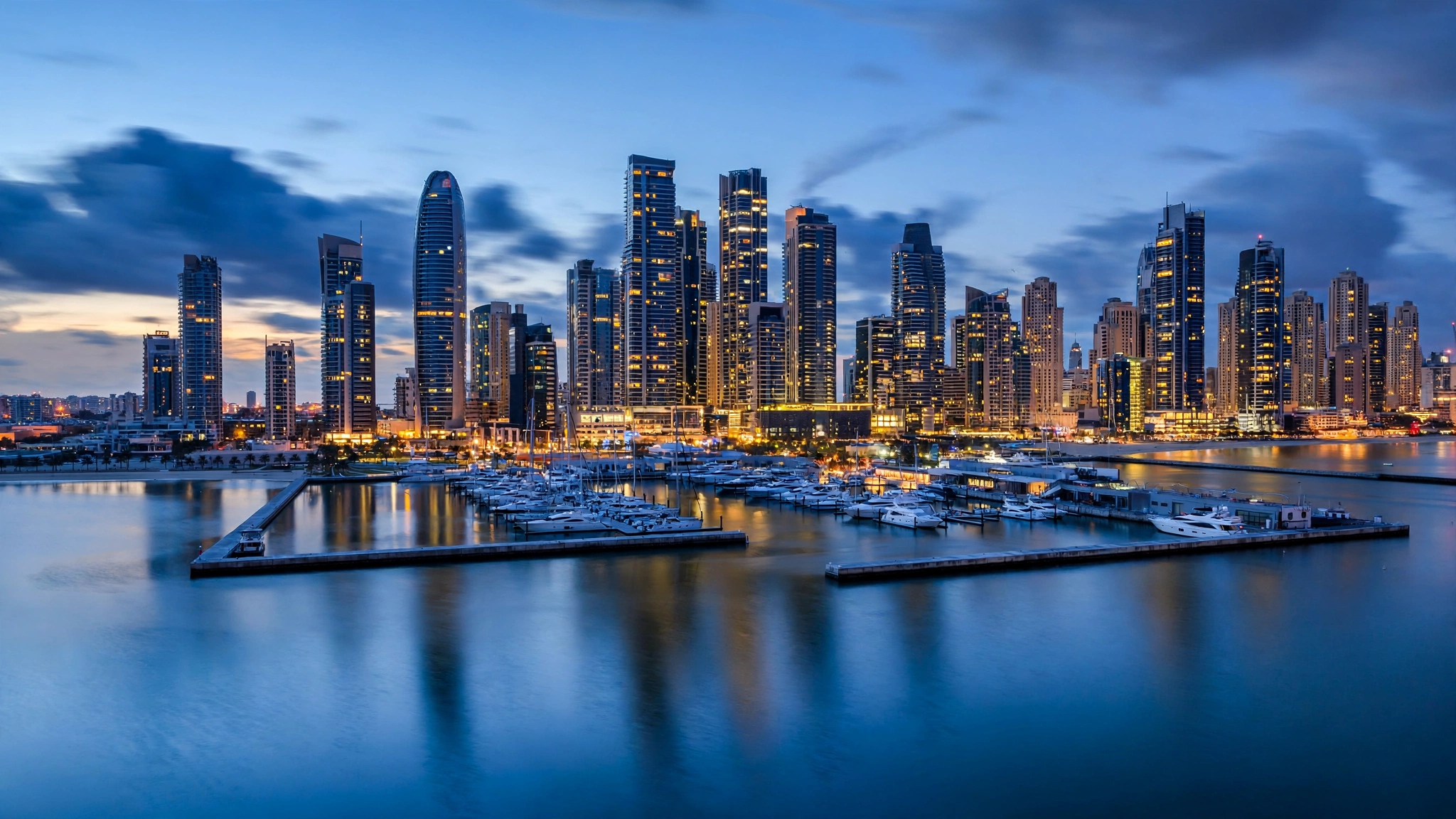 A modern coastal city skyline with high-rise towers and a marina at dusk