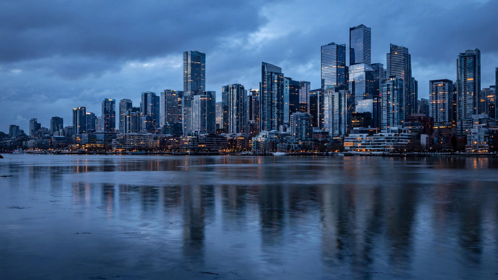 A modern city skyline with tall glass towers reflected in calm water at dusk