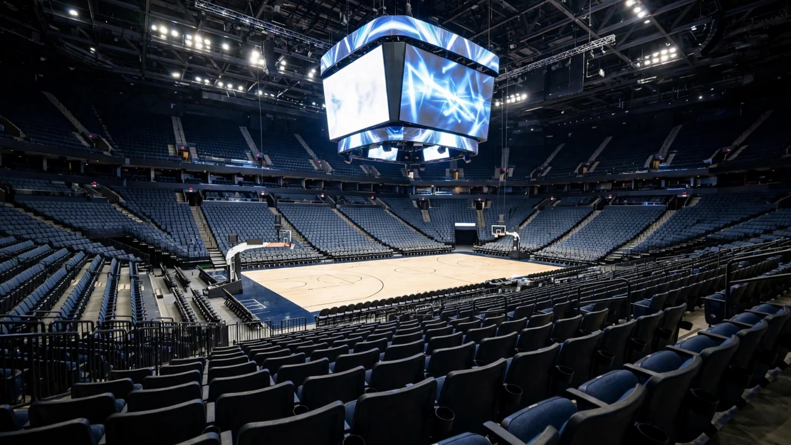 An empty indoor basketball arena with a large glowing video screen hanging above the court