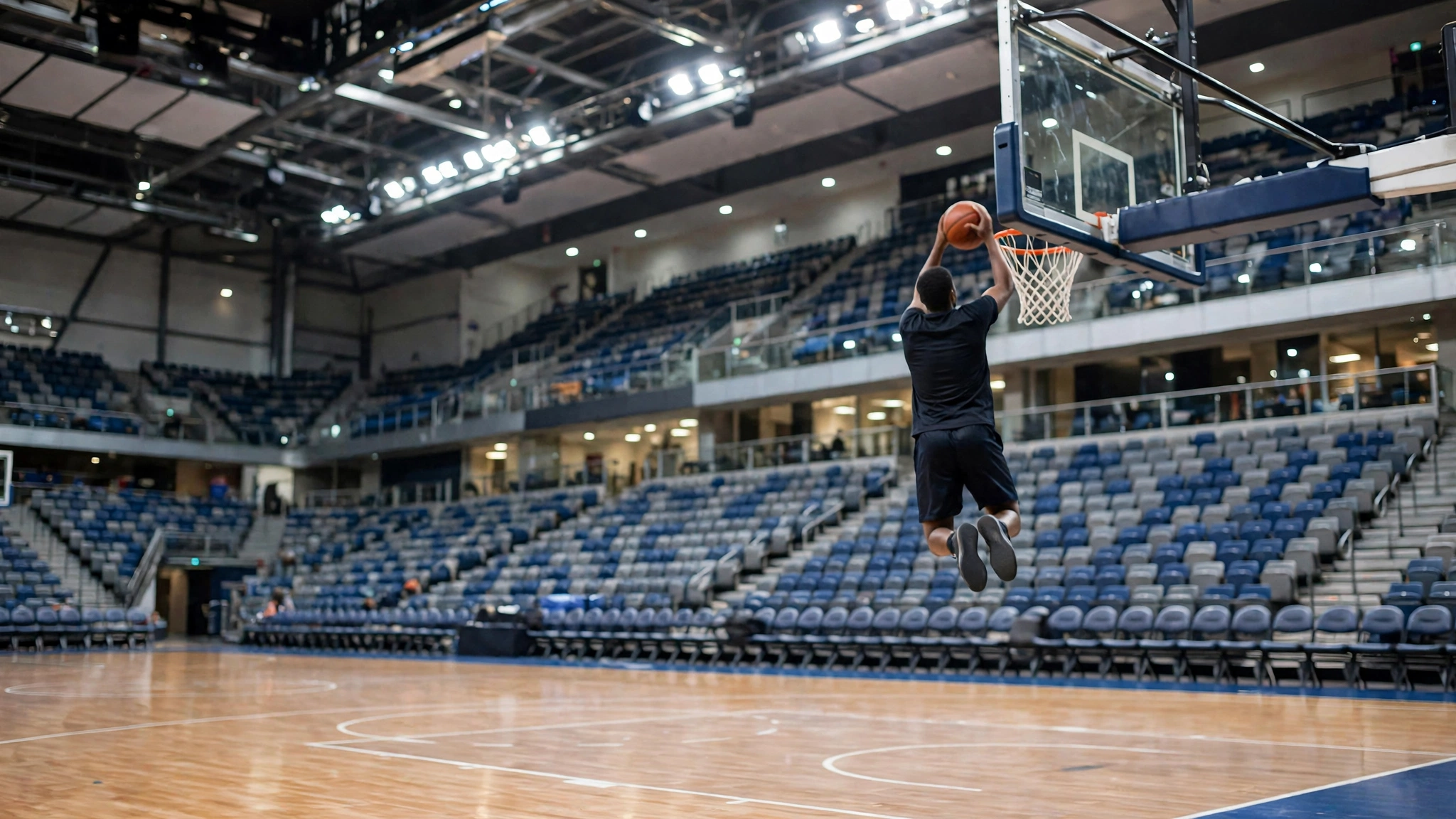 A basketball player in a plain dark jersey dunking a ball in a bright indoor arena, seen from behind
