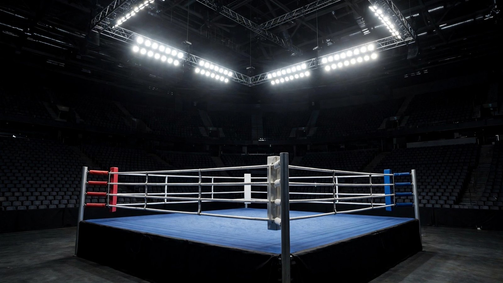 An empty boxing ring under bright arena lights in a dark arena