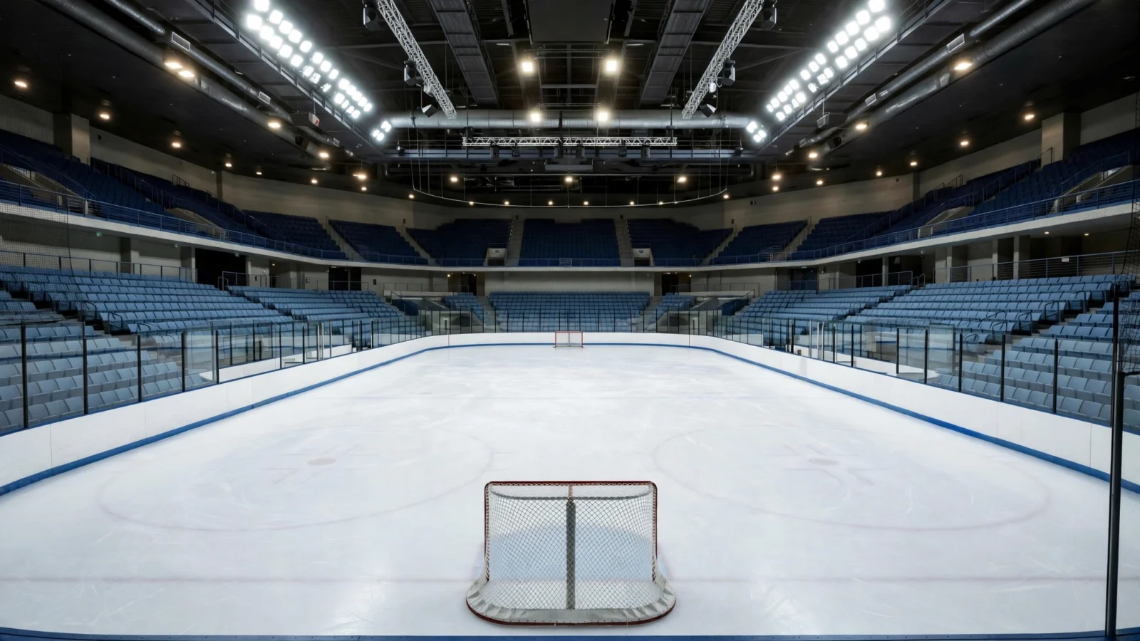 An empty indoor ice hockey arena with a clean ice rink, a goal net and rows of blue seats