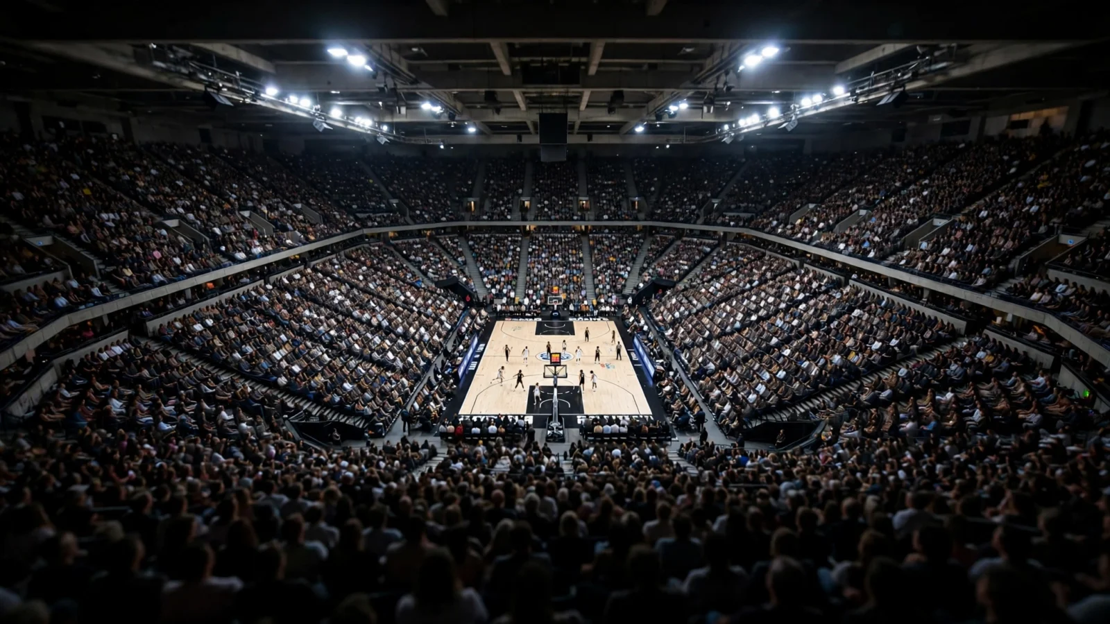 A packed indoor basketball arena at night with players on the court during a professional game