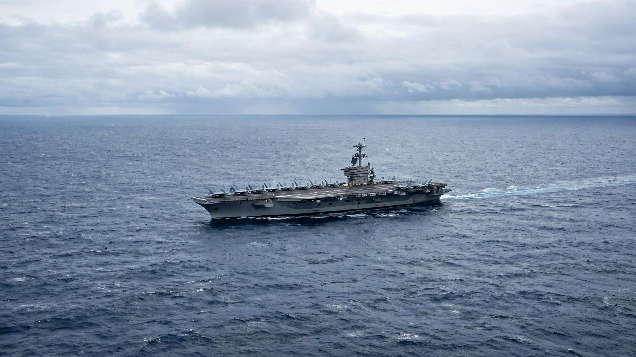 Fighter jets parked on the flight deck of an aircraft carrier sailing in open ocean