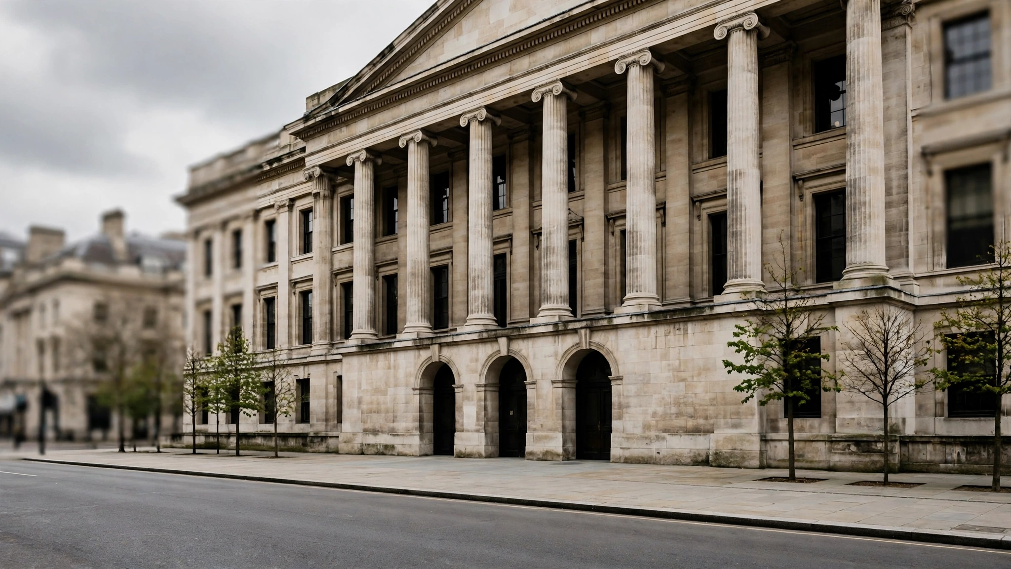 A stone building with tall columns and arched doorways beside an empty street
