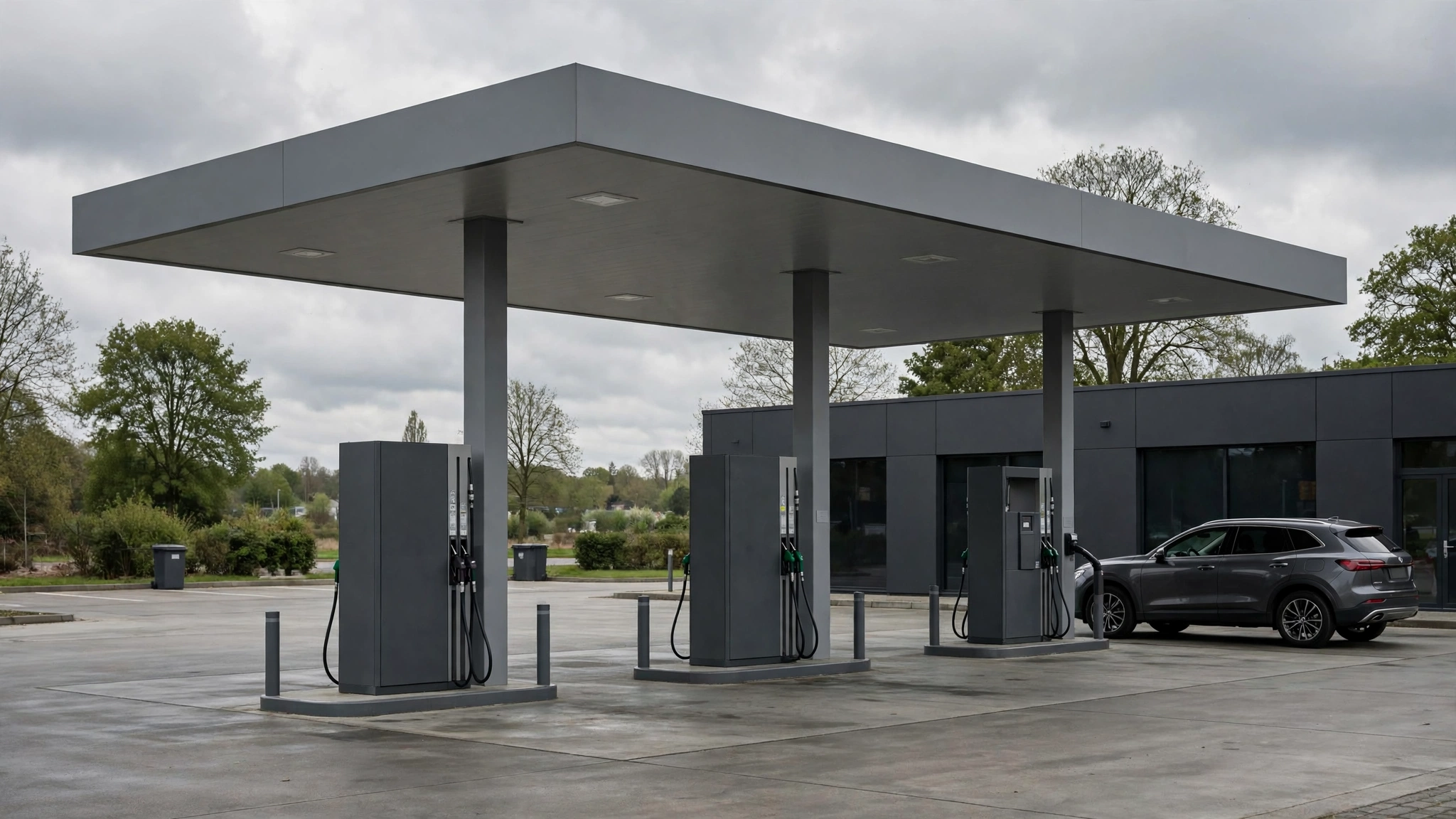 Fuel pumps under a canopy at a gas station, with a car parked beside a low building