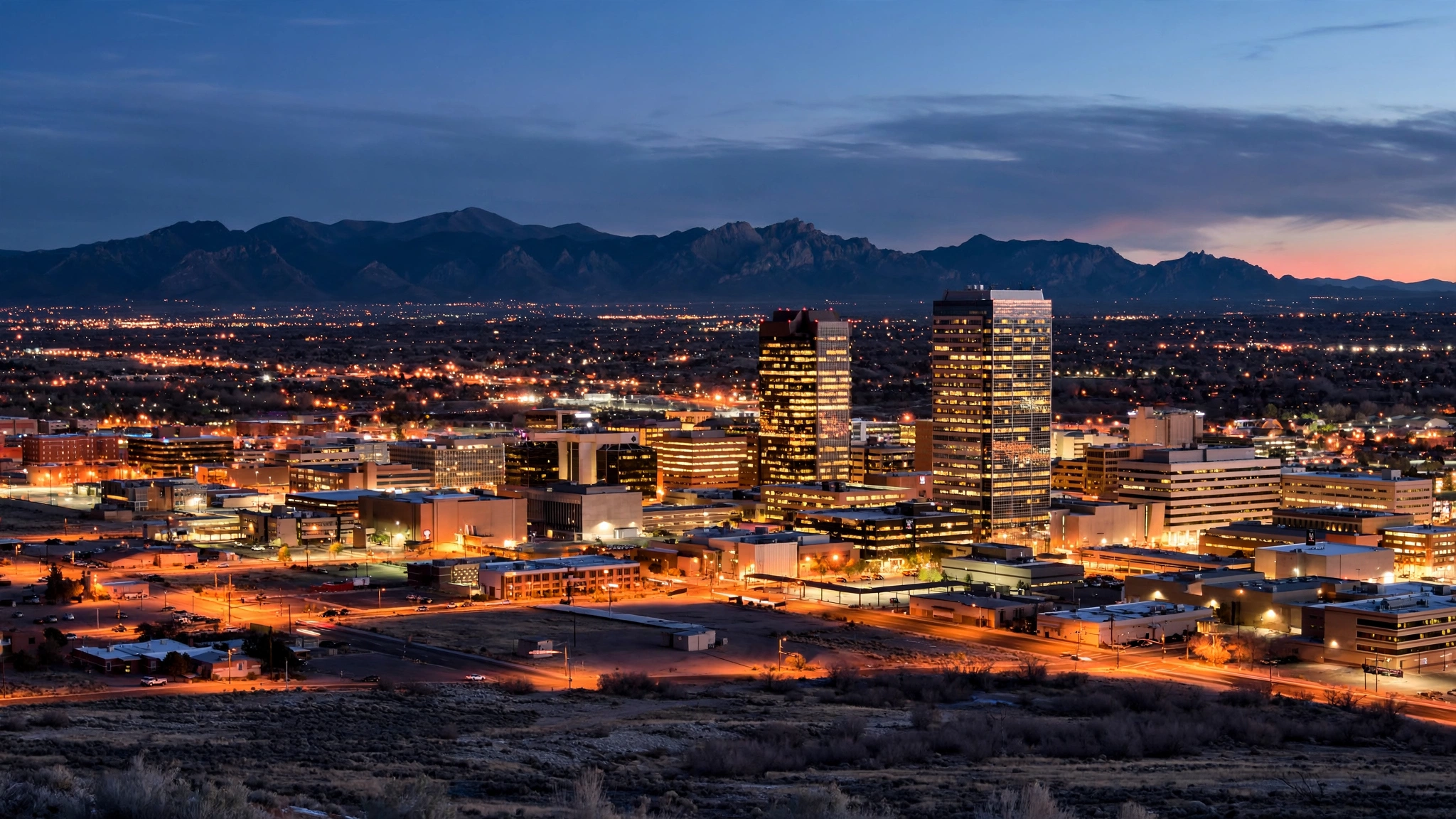 The downtown Albuquerque skyline at dusk with mountains in the distance.