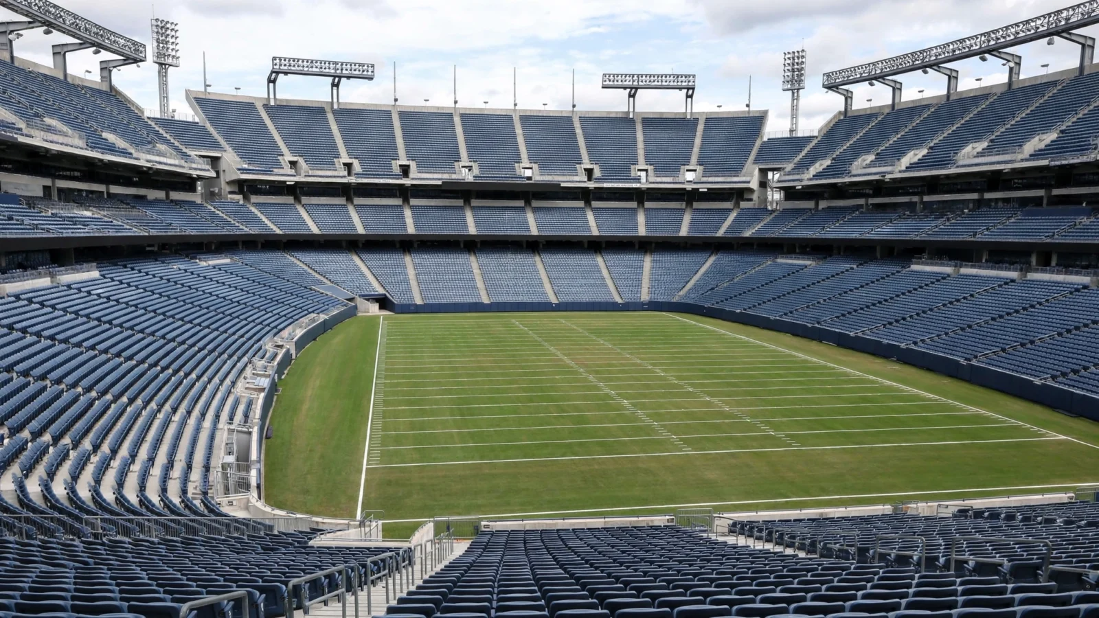 An empty football stadium with rows of blue seats around a green field marked with white yard lines