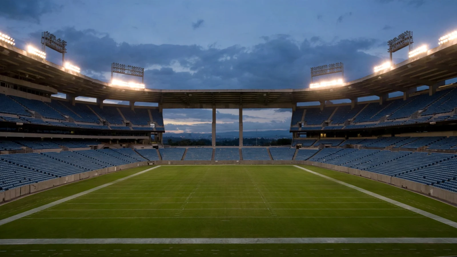 An empty football stadium lit by floodlights at dusk