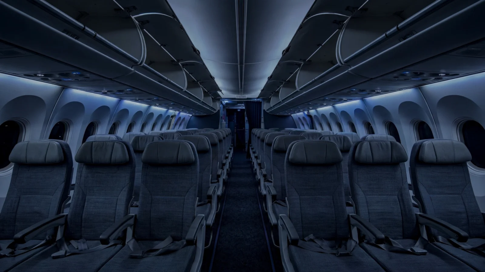 The dimly lit cabin of a commercial airliner at night, viewed down the aisle between rows of empty seats.