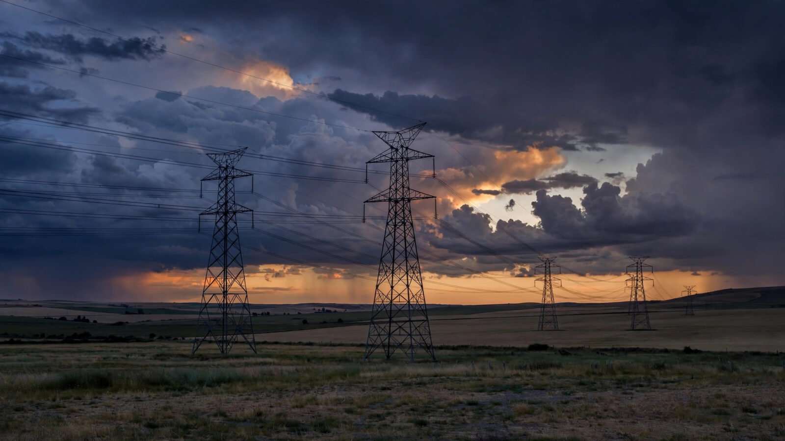 High-voltage electricity transmission towers silhouetted against a stormy dusk sky.