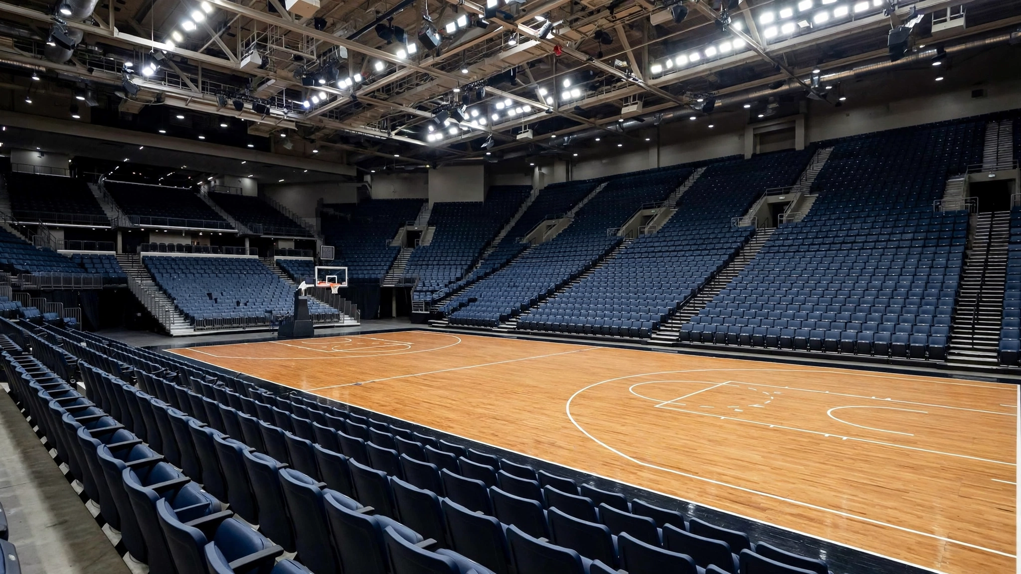 An empty basketball court with wooden flooring and rows of dark blue seats in an arena