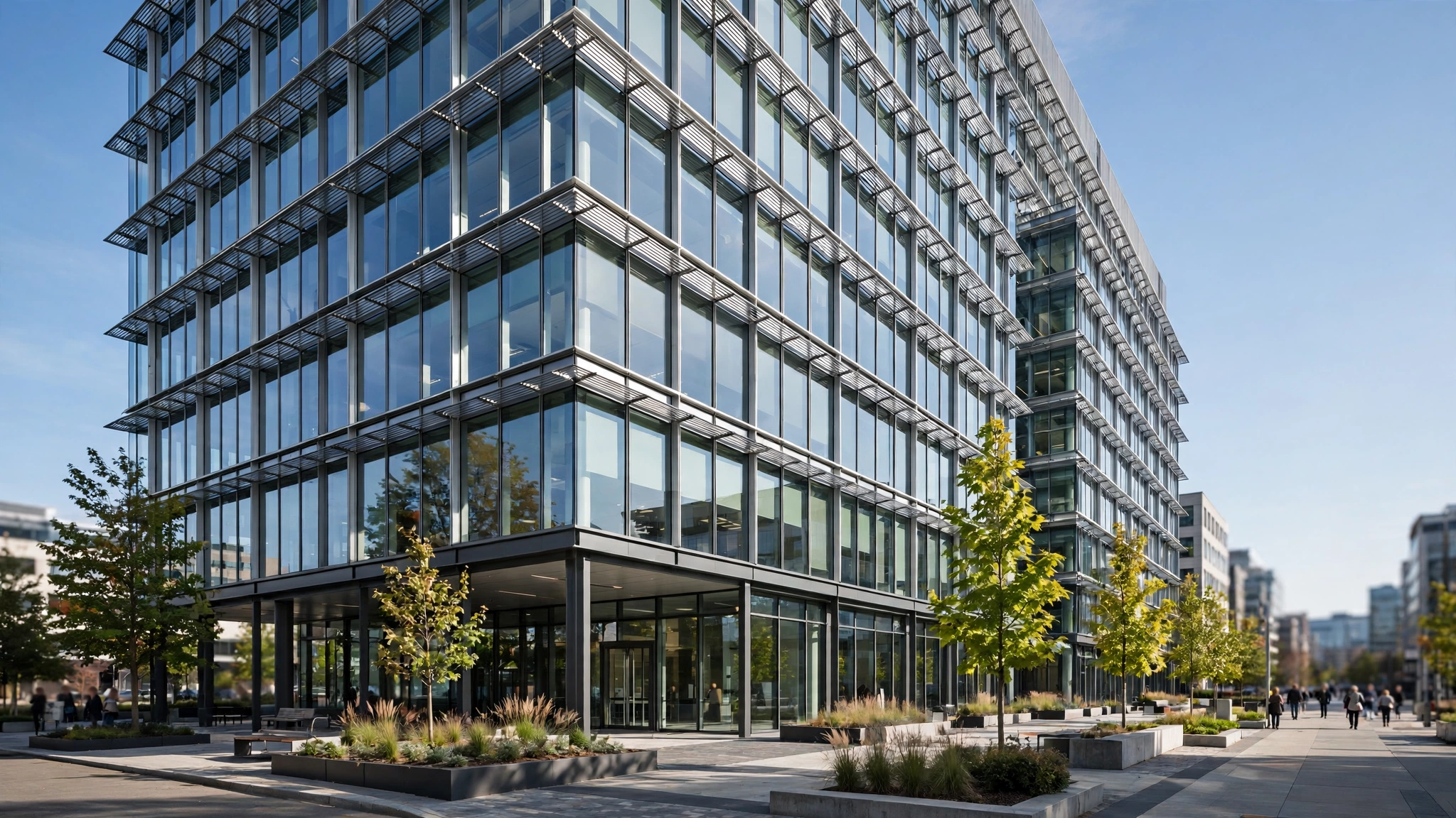 A modern glass office building exterior on a sunny day, with pedestrians walking at a distance