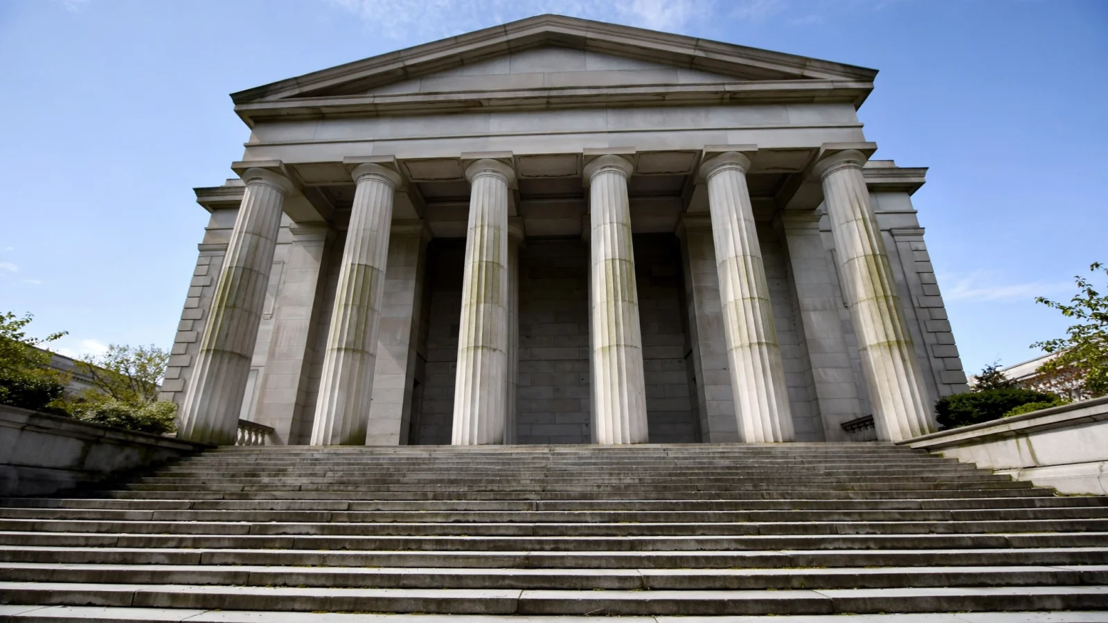 Stone columns and wide steps of a federal courthouse building under a clear blue sky.