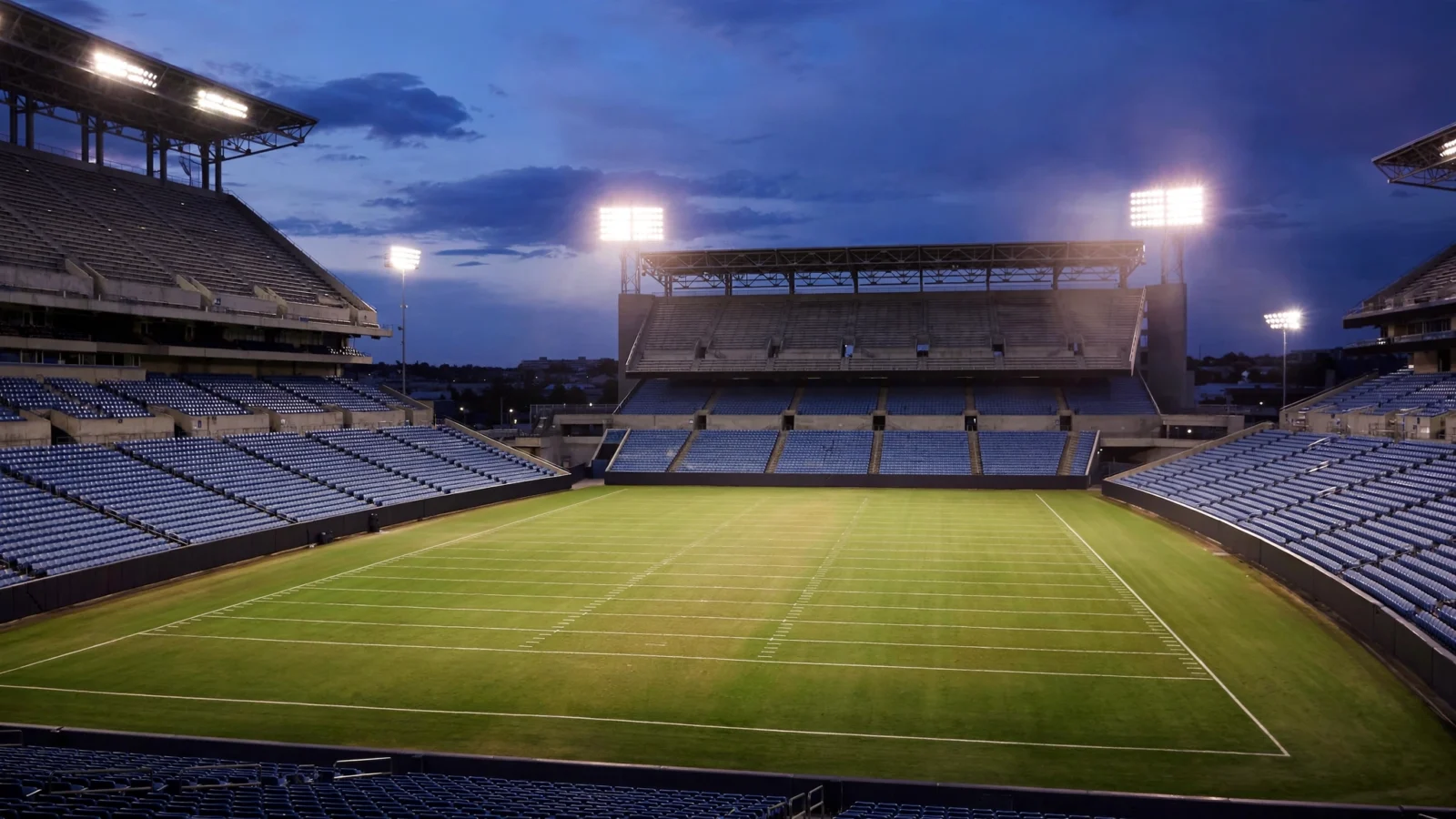 An empty American football stadium at dusk with floodlights on