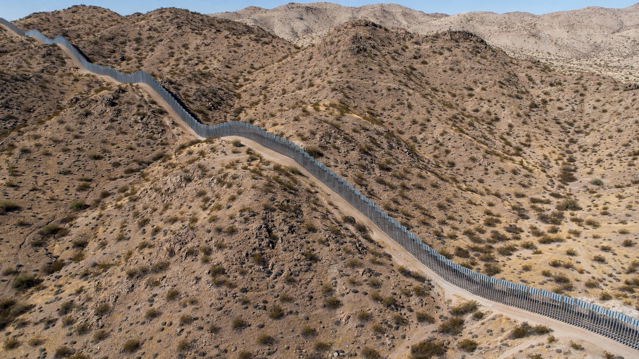 Aerial view of a steel border barrier winding through desert hills