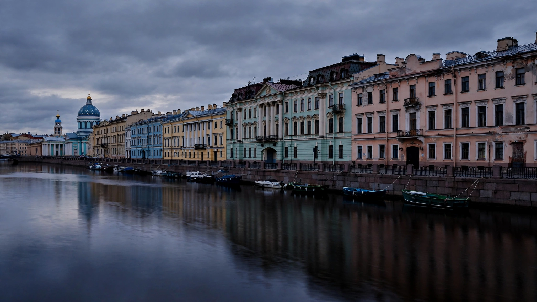 Historic buildings along a canal in St. Petersburg, Russia, at dusk, with boats moored on the dark water.