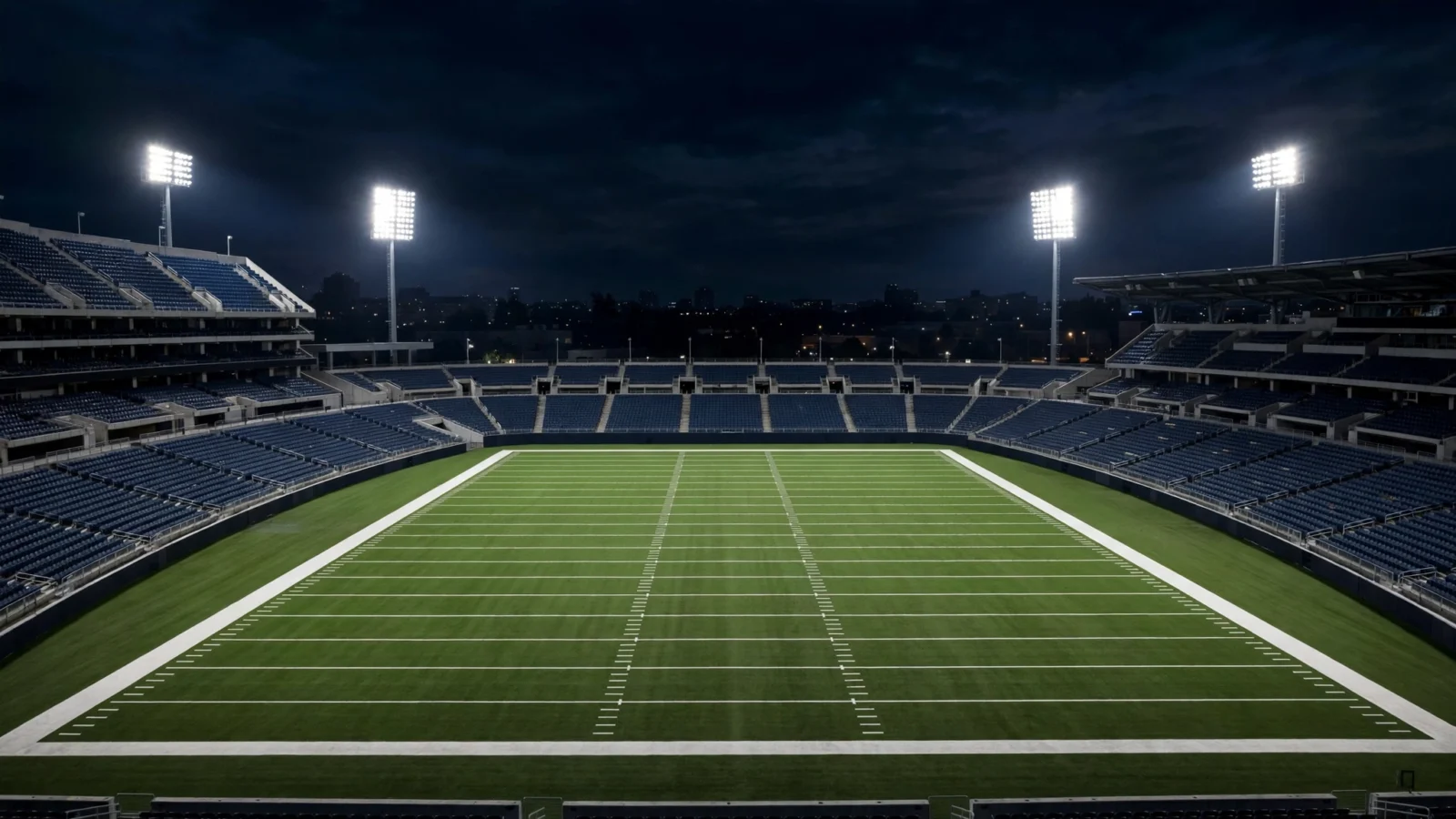 An empty American football stadium with a lit green field at night.