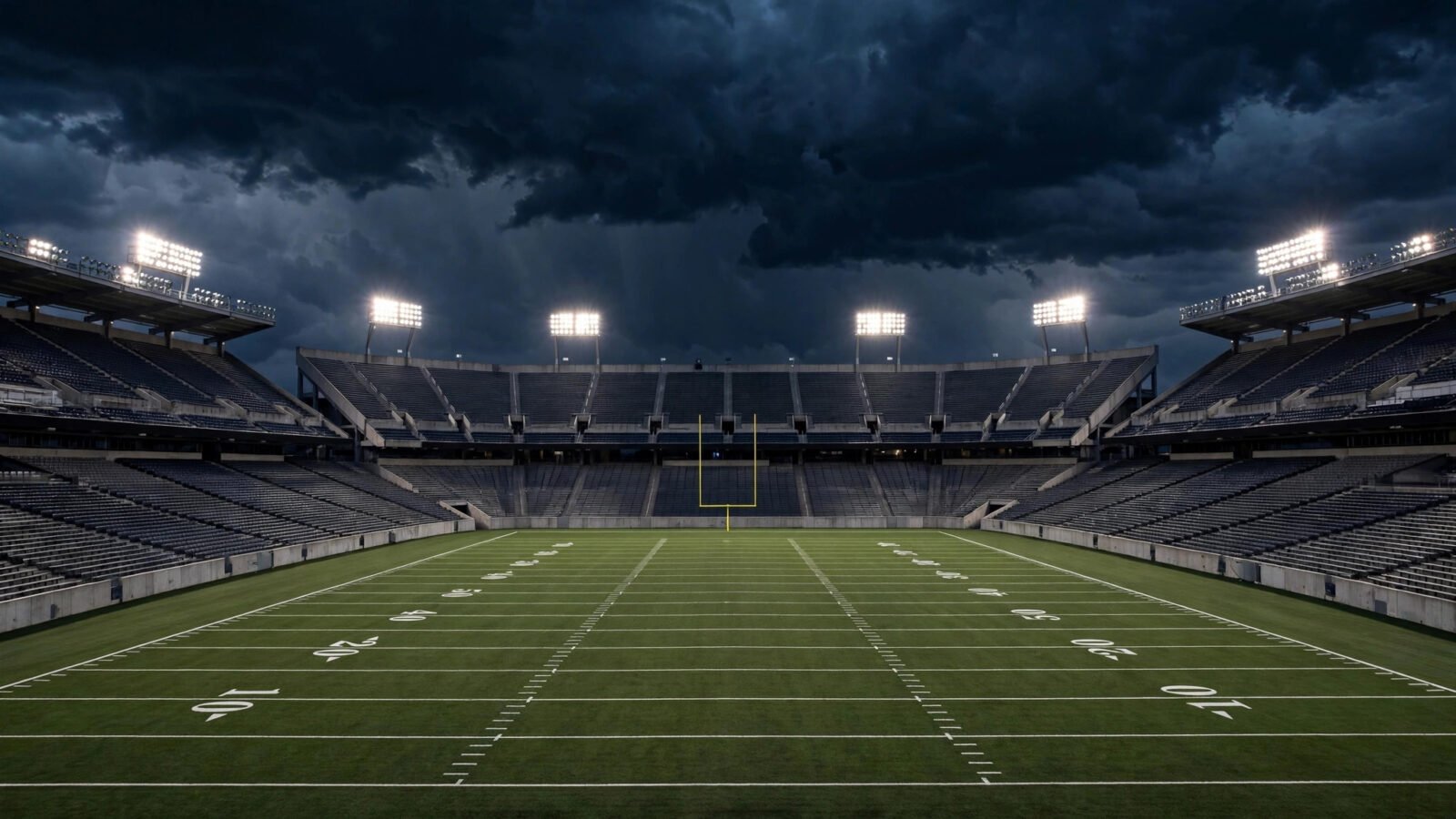 An empty American football stadium at night under bright floodlights, with yard lines and a goalpost on the field.