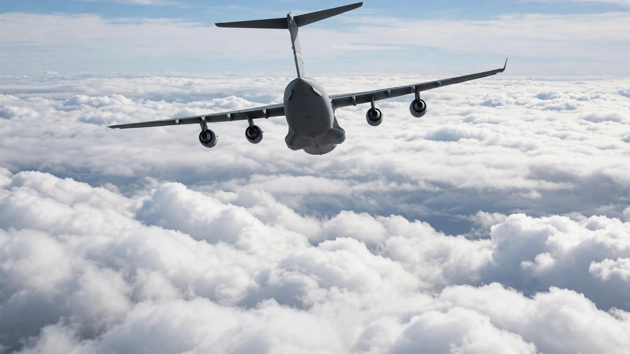 A large military cargo aircraft flying above a layer of clouds.