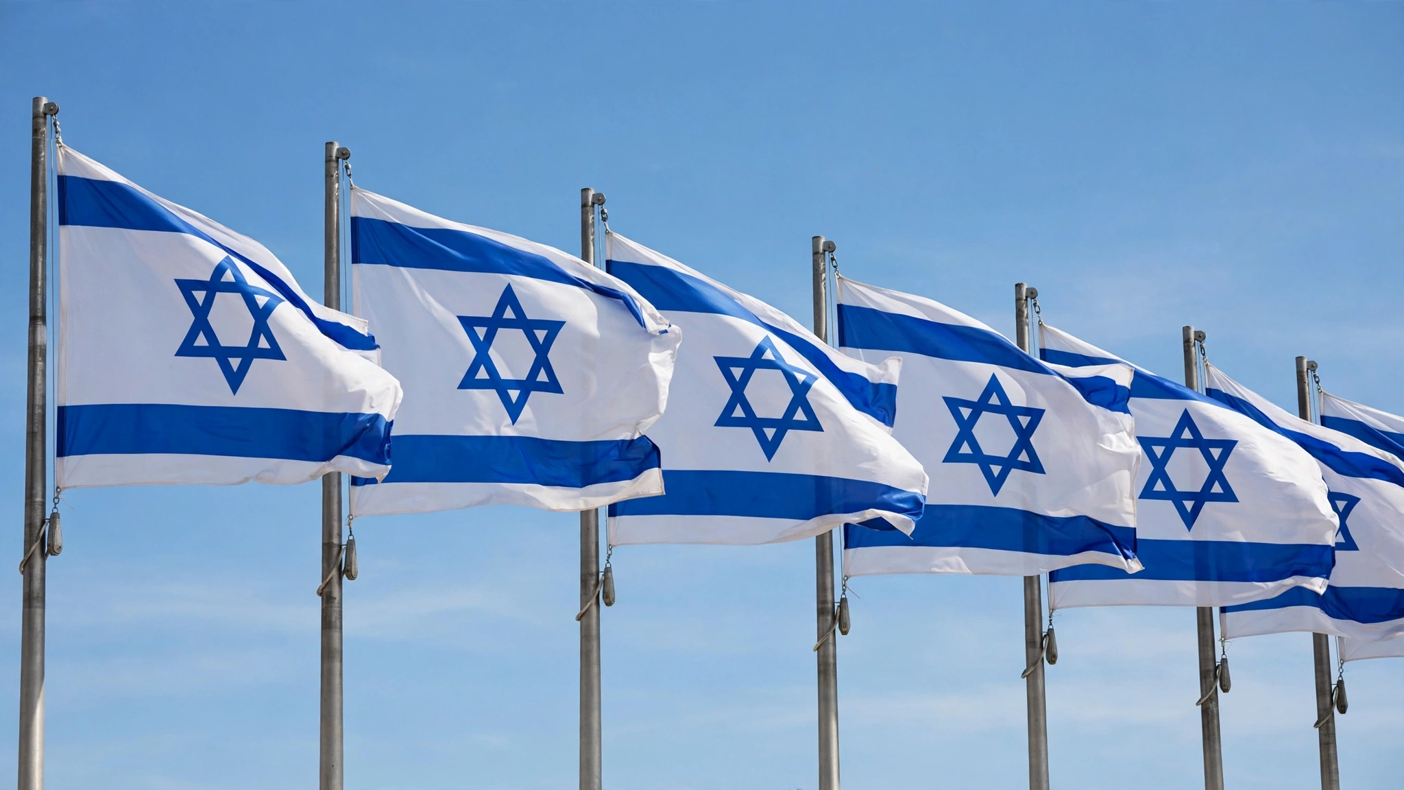 Israeli flags with blue Stars of David waving on flagpoles against a clear blue sky