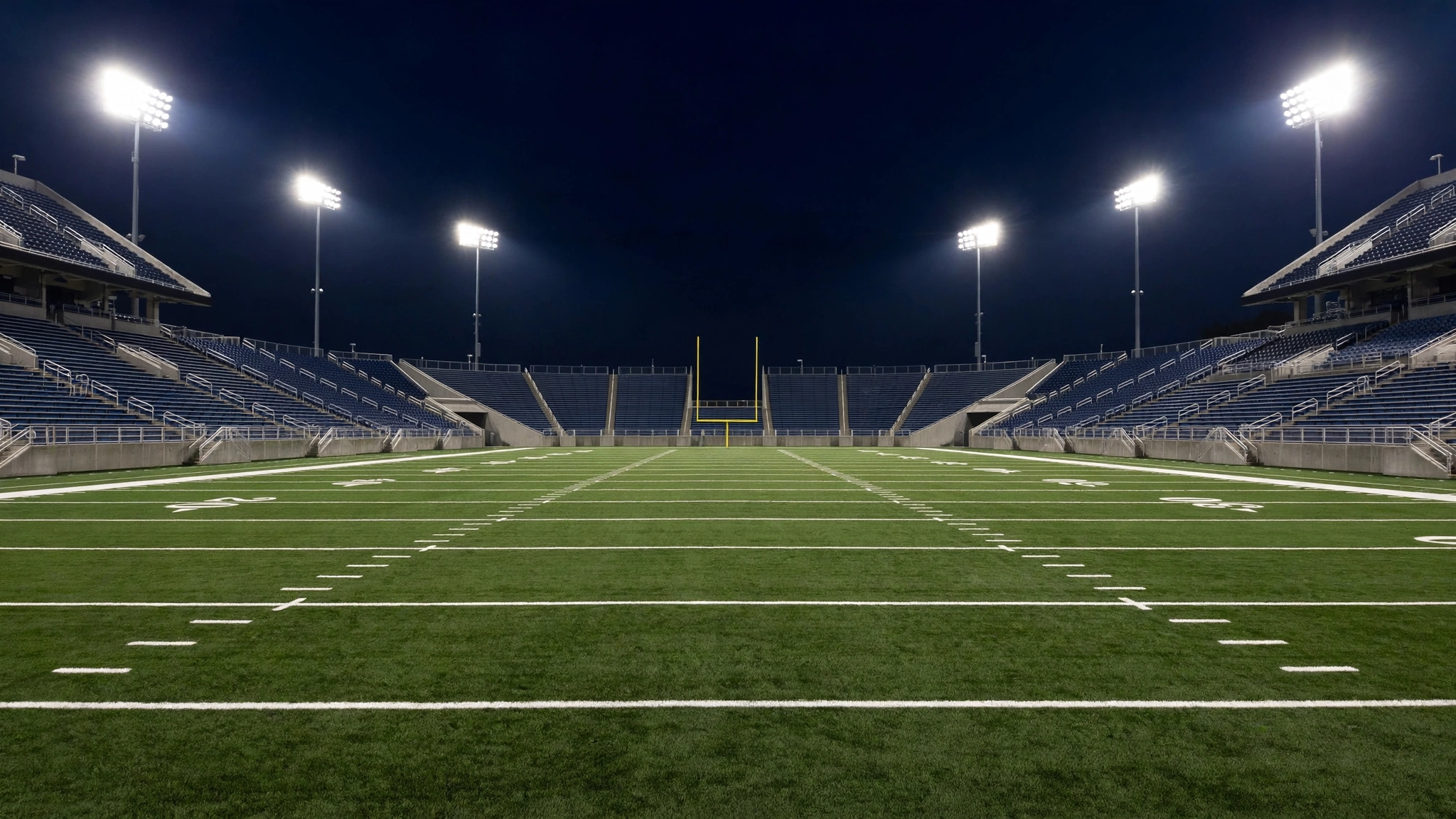 An empty American football field under bright stadium lights at night, with goal posts at the far end