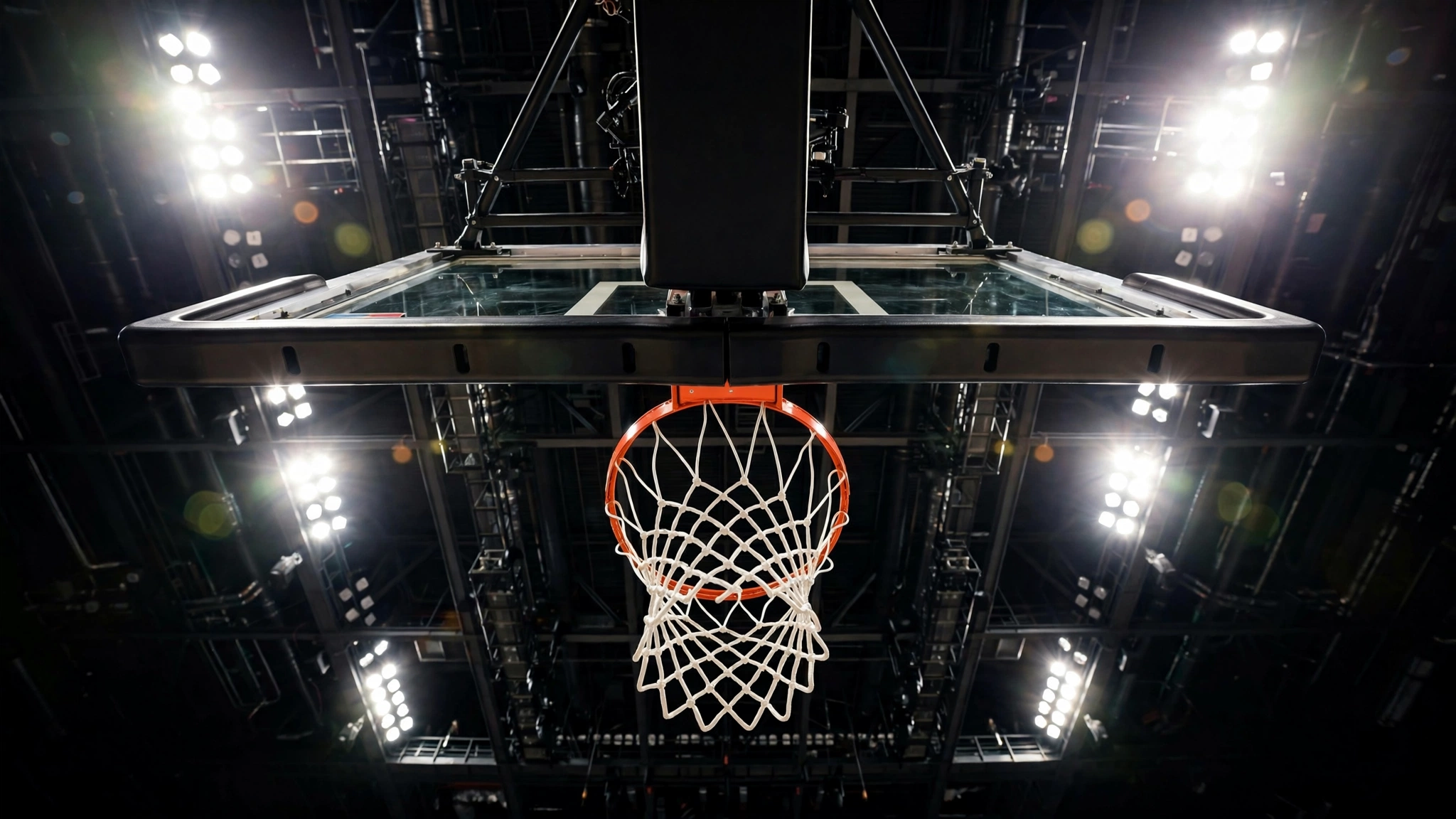 A basketball hoop and backboard viewed from below against bright arena lights